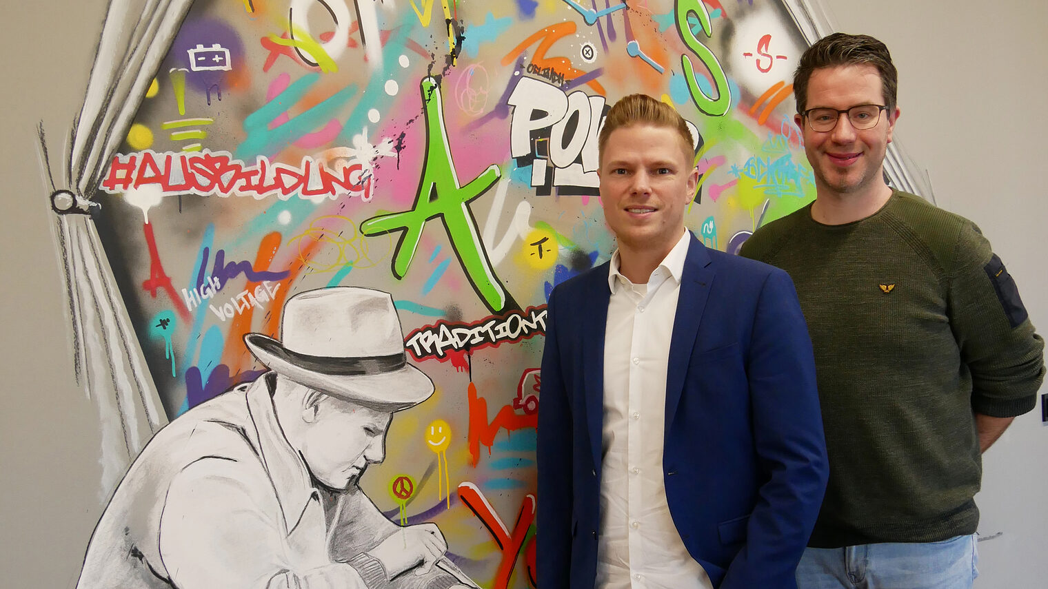 (v.l.) Thomas Beckhoff, Projektleiter Gebäudeautomation, und Ausbildungsmeister Thomas Erdbories vor einem Graffiti im Ausbildungszentrum