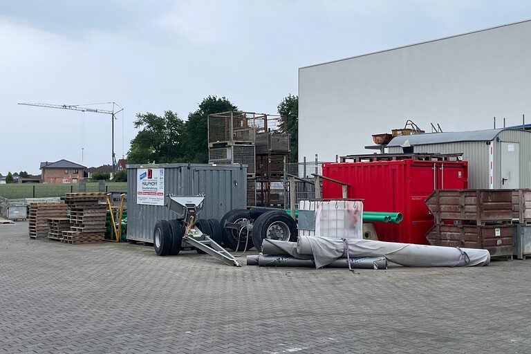 Reifen, Container, Metall und Holzplatten draußen auf dem Boden vor einer Halle 