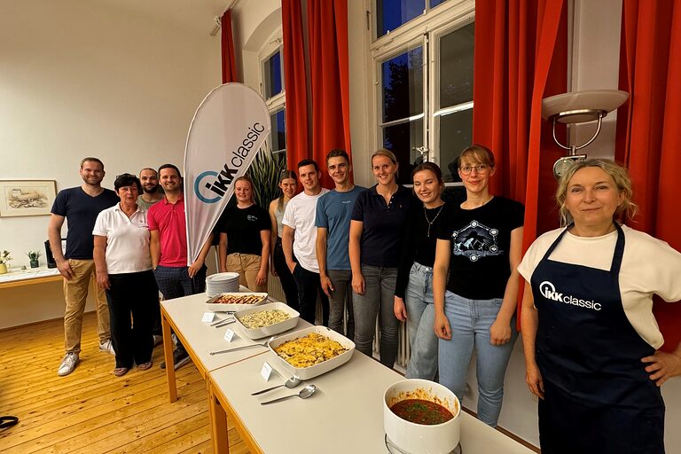Gruppe von Leuten in einer Reihe, welche vor frischem Essen stehen.