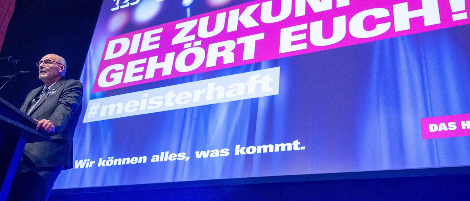 Präsident Peter Eul steht vor einem Bildschirm "Die Zukunft gehört euch!" und hält eine Rede für die Meister:innen. 