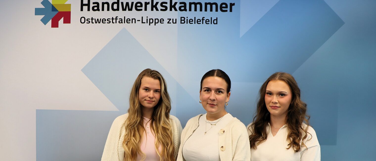 Drei Auszubildende von der Handwerkskammer OWL vor einer blauen Fotowand 