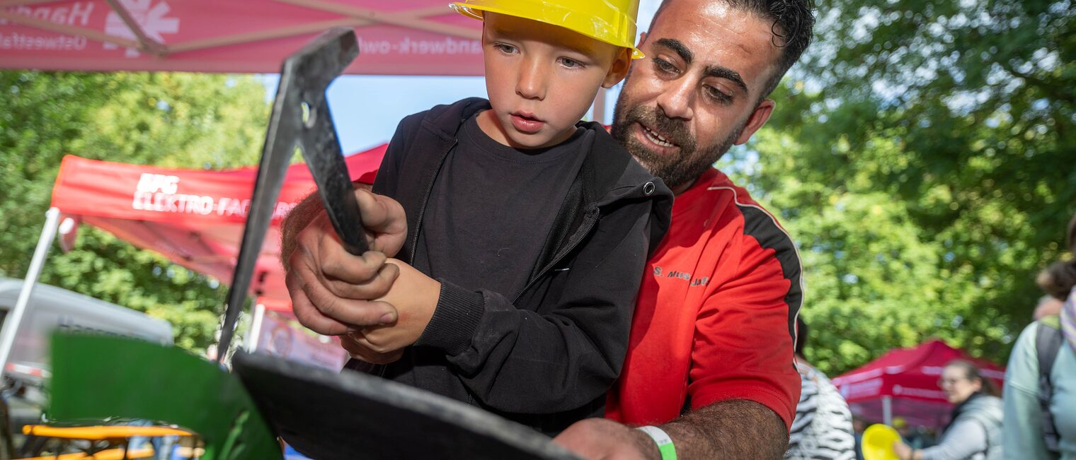 Kind mit Werkzeug bearbeitet mit Hilfe eines Handwerkers eine Schiefernplatte.