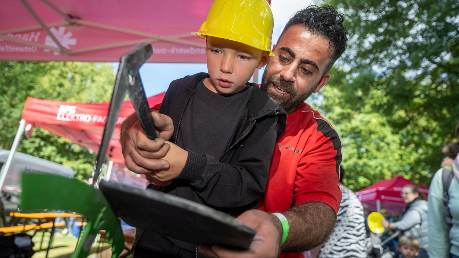 Kind mit Werkzeug bearbeitet mit Hilfe eines Handwerkers eine Schiefernplatte.