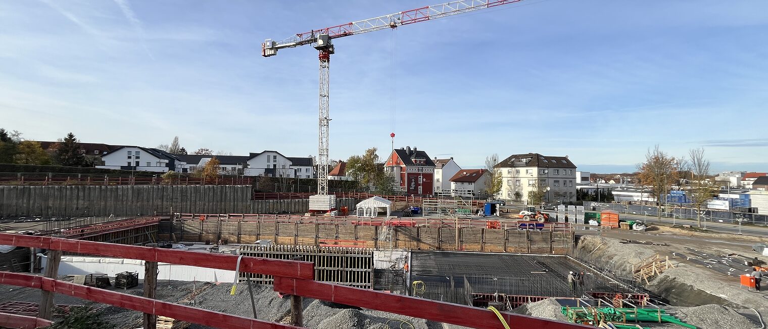 Die Baustelle am Neubau am Campus Handwerk geht voran. Zu sehen sind ein roter Bauzaun und ein Kran. 