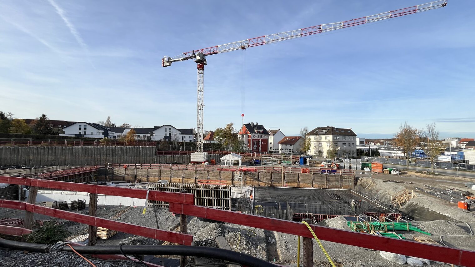 Die Baustelle am Neubau am Campus Handwerk geht voran. Zu sehen sind ein roter Bauzaun und ein Kran. 