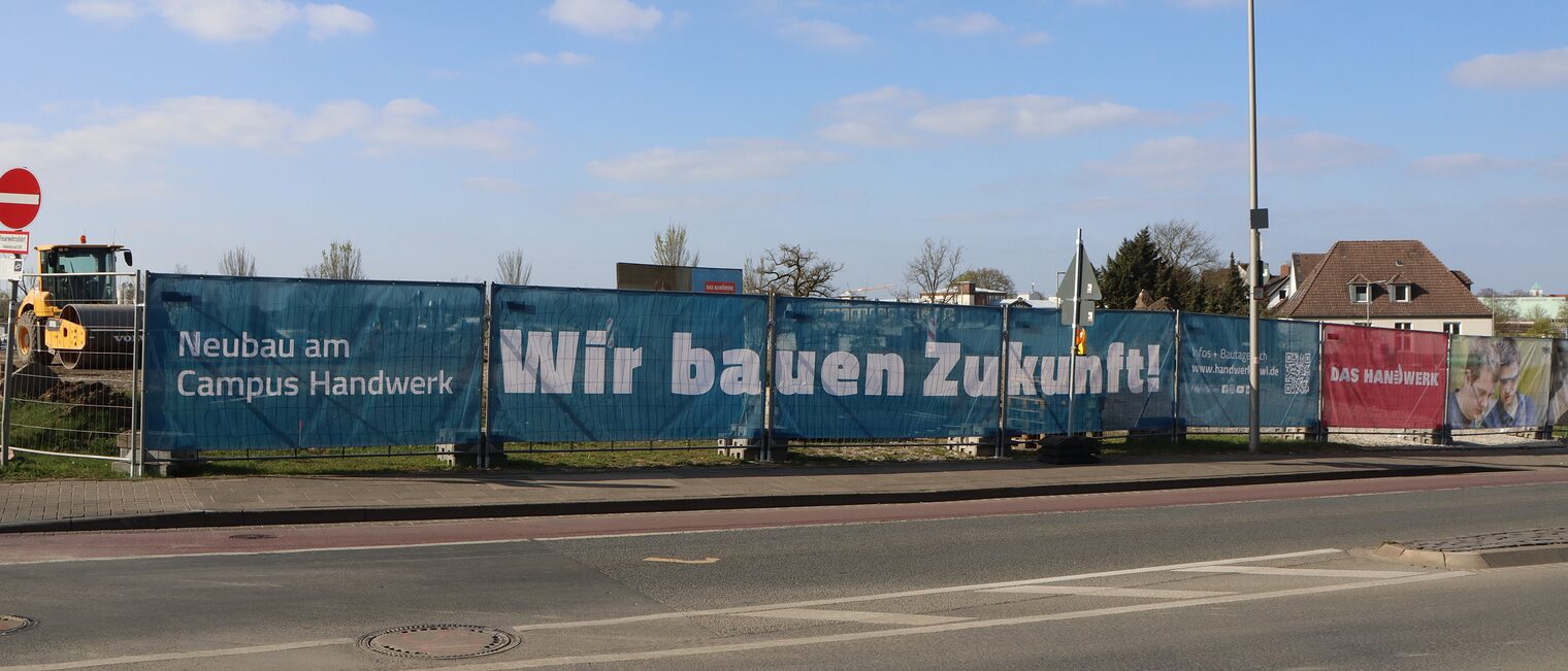 "Wir bauen Zukunft" steht auf einem Banner vor der Baustelle am Campus Handwerk. 