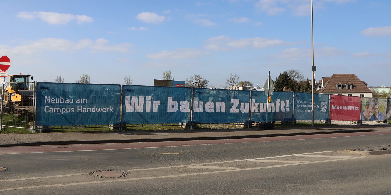 "Wir bauen Zukunft" steht auf einem Banner vor der Baustelle am Campus Handwerk. 