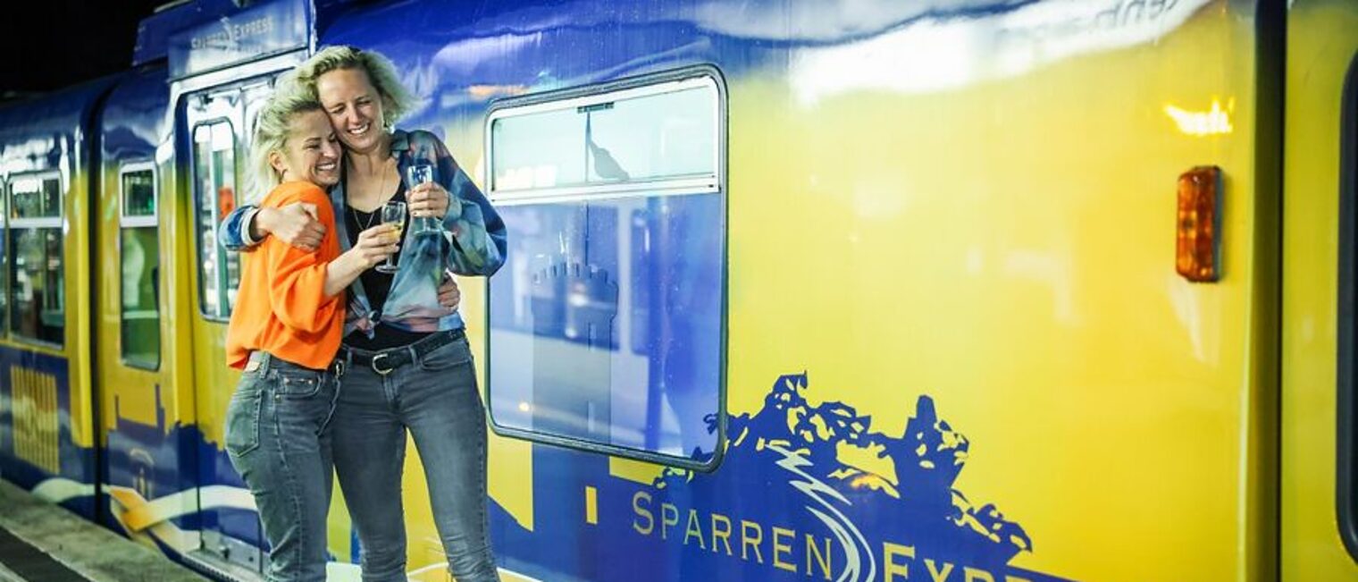 zwei Personen liegen sich freudig in den Armen. Dahinter der Sparrenexpress