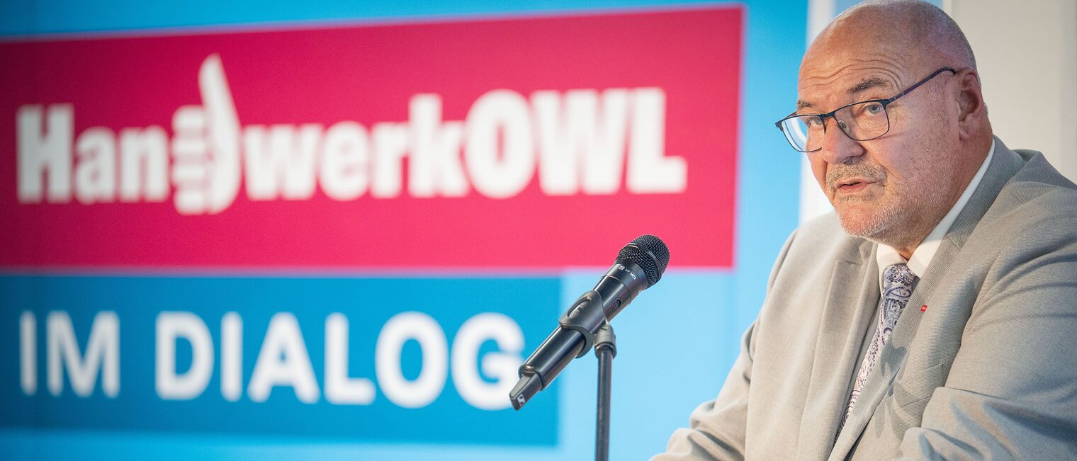 Präsident Peter Eul steht vor einer Wand mit dem Aufdruck "Handwerk OWL im Dialog".
